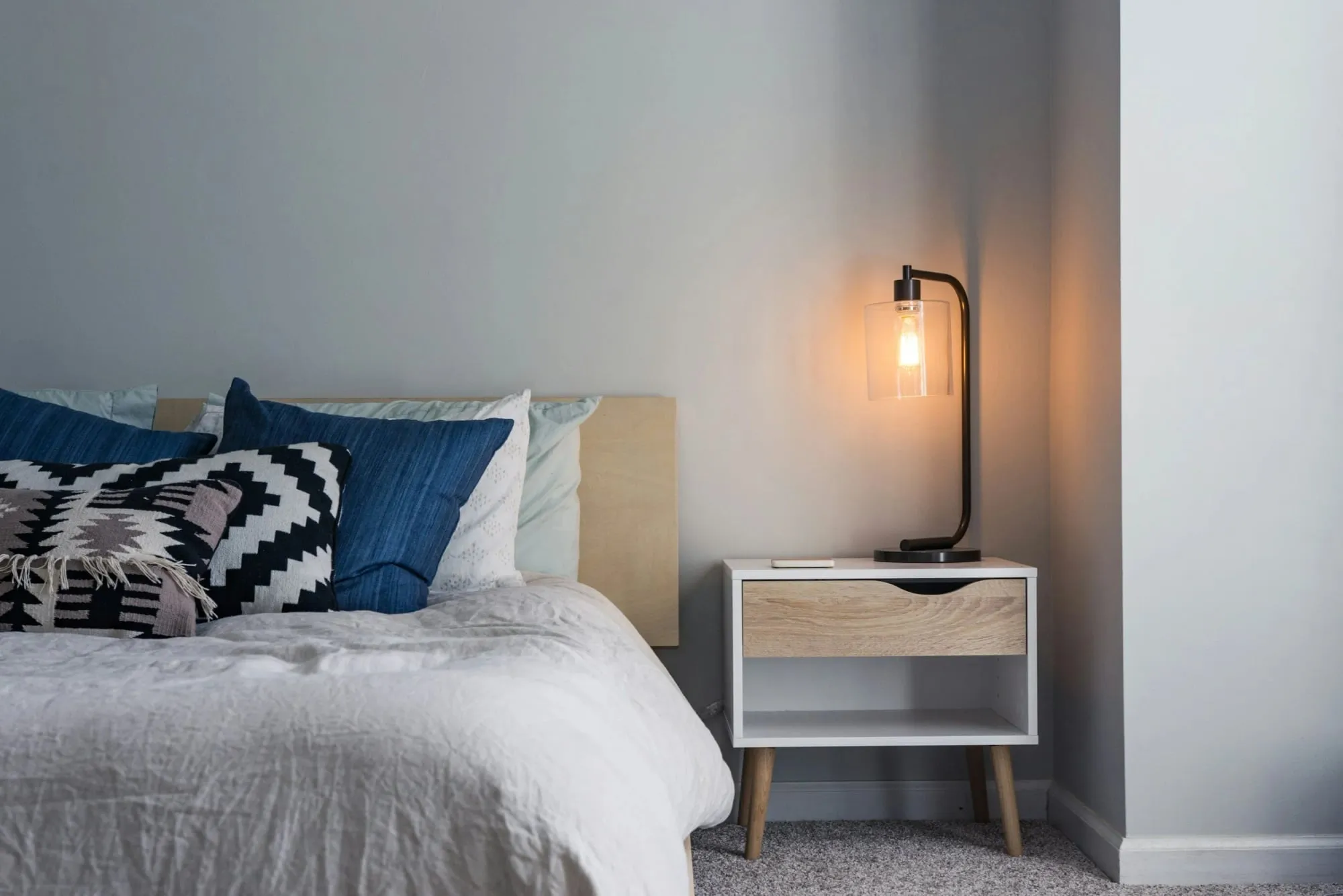 A cosy hotel bedroom with a made bed and a warm bedside lamp.
